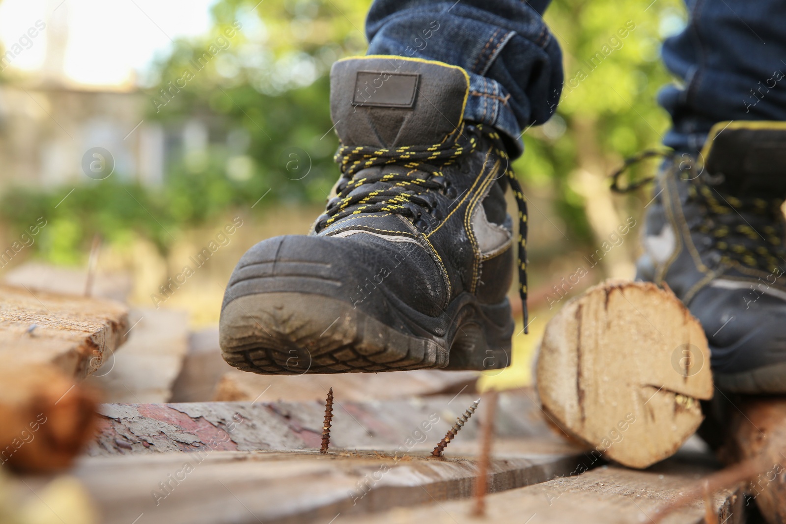 Photo of Careless worker stepping on nail in wooden plank outdoors, closeup