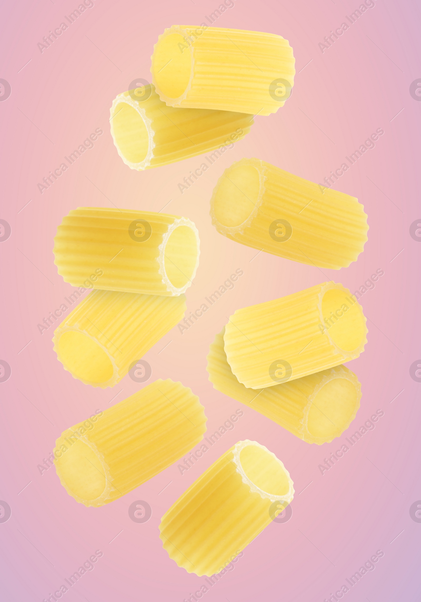 Image of Raw rigatoni pasta falling on pink background