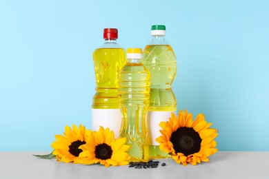 Photo of Bottles of cooking oil, sunflowers and seeds on white table