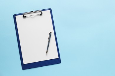 Photo of Ballpoint pen and clipboard with paper sheet on light blue background, top view. Space for text