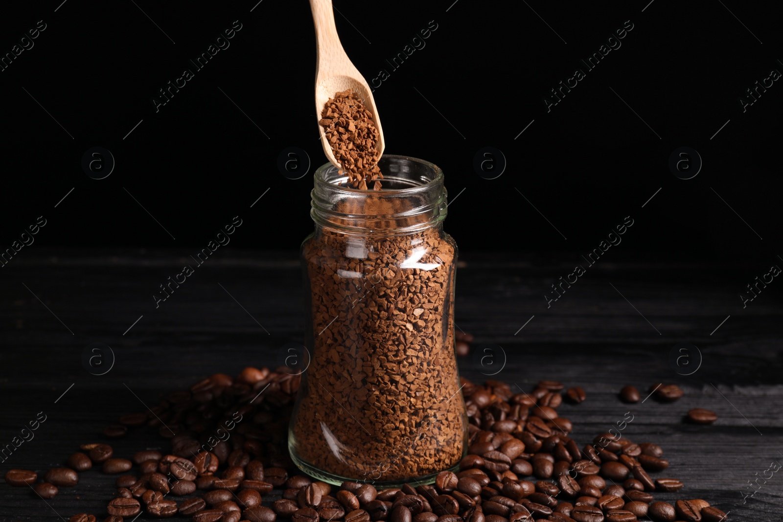 Photo of Putting instant coffee into glass jar on black wooden table