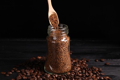Photo of Putting instant coffee into glass jar on black wooden table