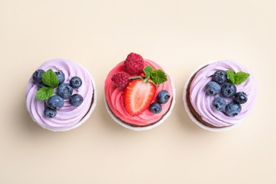 Different delicious cupcakes with cream and berries on beige background, flat lay