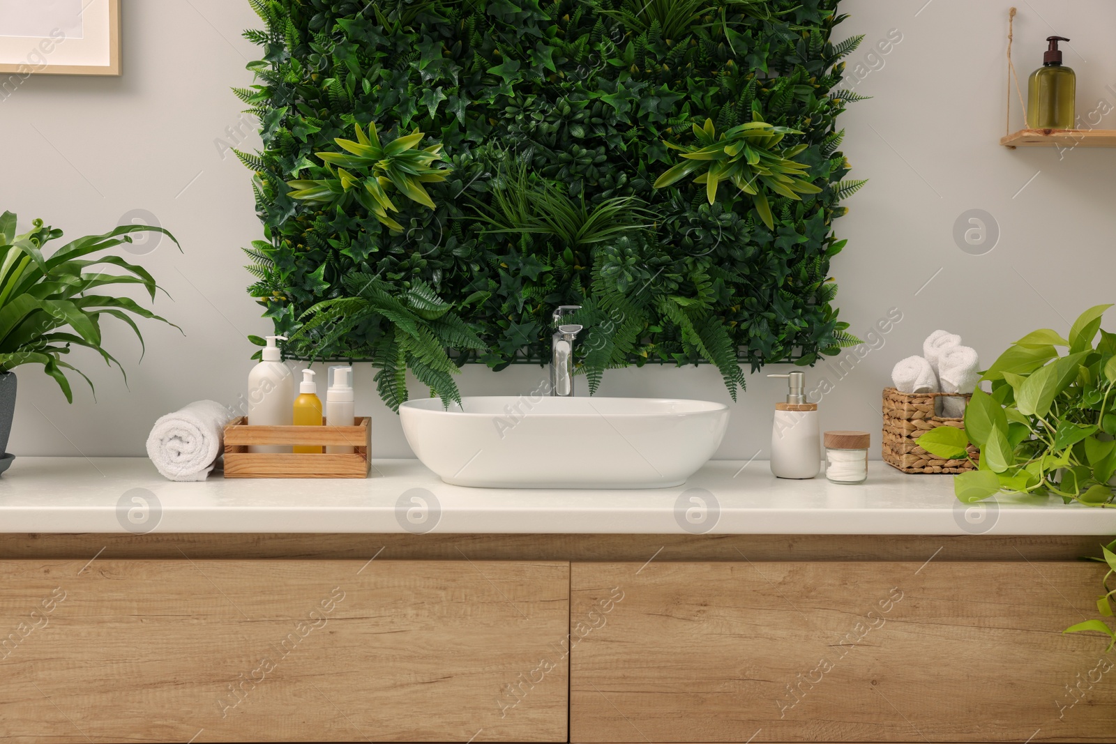 Photo of Green artificial plants, vanity and different personal care products in bathroom