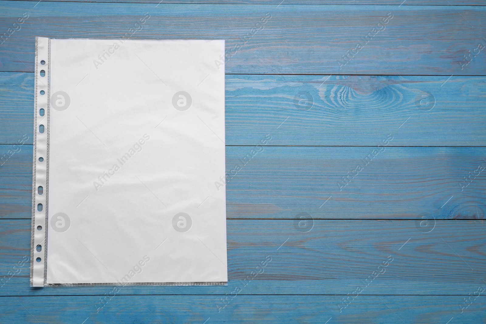 Photo of Punched pocket with paper sheet on light blue wooden table, top view. Space for text