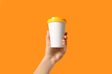 Photo of Woman holding takeaway paper coffee cup on orange background, closeup