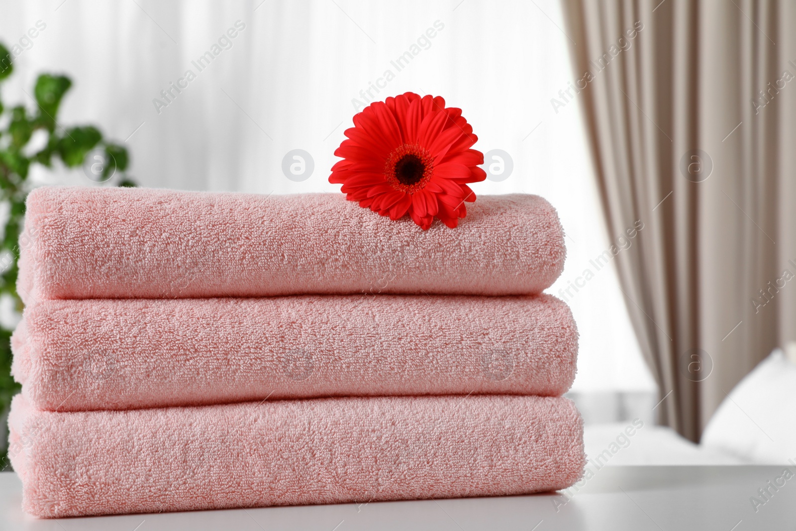 Photo of Stack of fresh towels with flower on table in bedroom. Space for text