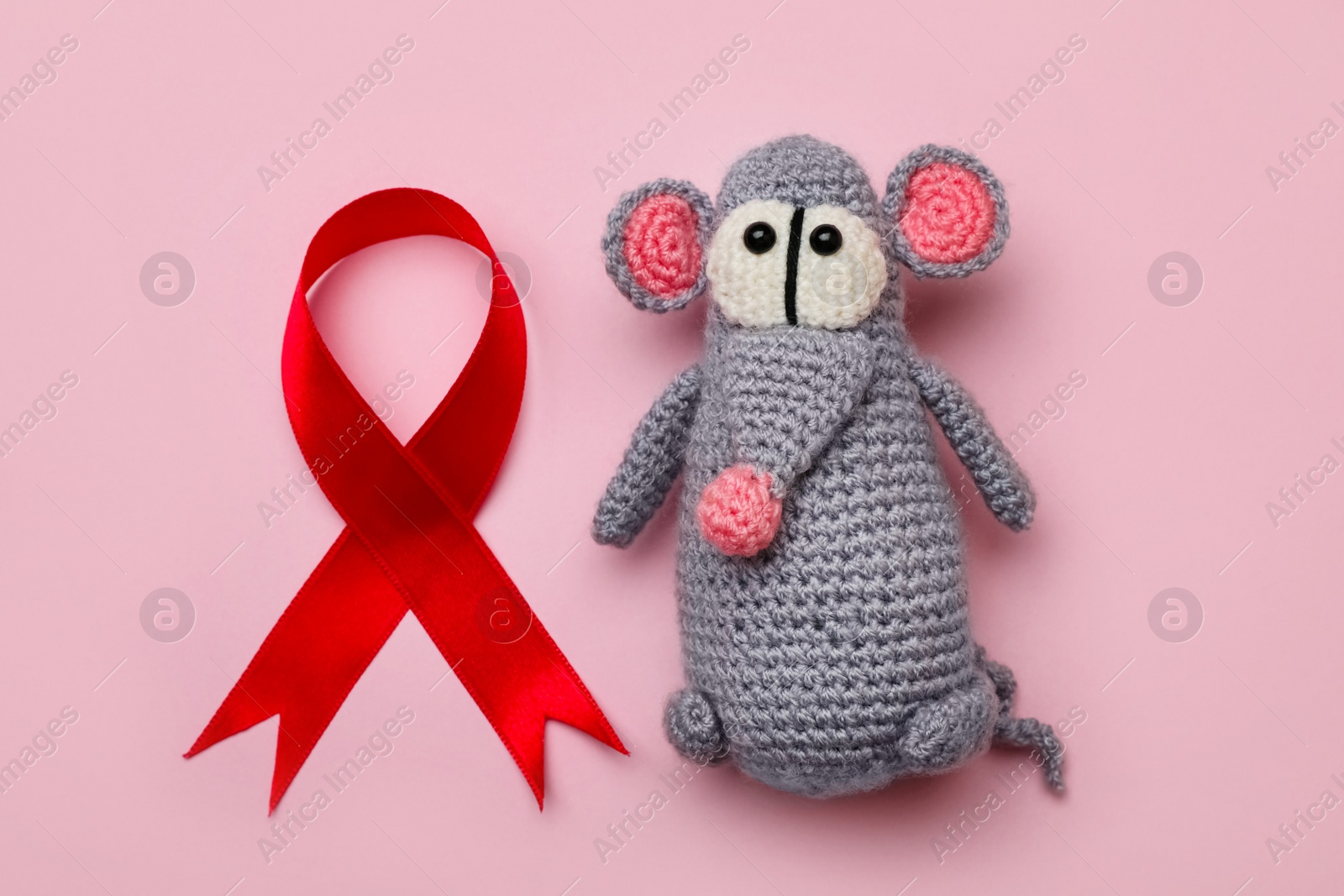 Photo of Cute knitted toy mouse and red ribbon on pink background, flat lay. AIDS disease awareness