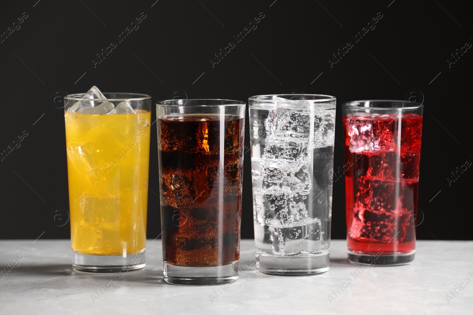 Photo of Glasses of different refreshing soda water with ice cubes on white marble table