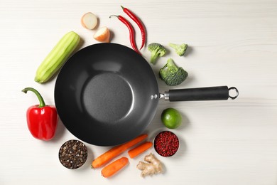 Photo of Empty iron wok surrounded by raw ingredients on white wooden table, flat lay