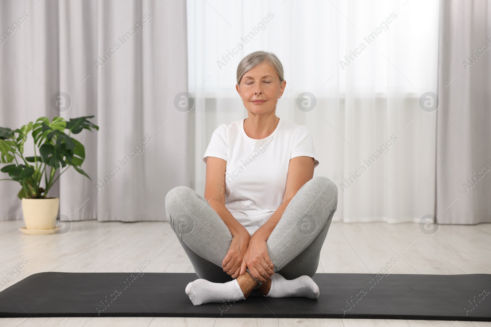 Photo of Senior woman practicing yoga on mat at home