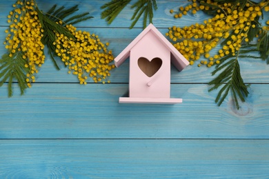 Stylish bird house and fresh mimosas on light blue wooden background, flat lay. Space for text