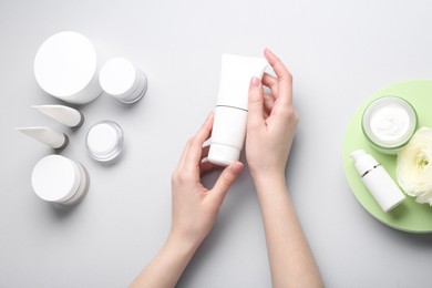 Woman holding tube of cream on light background, top view