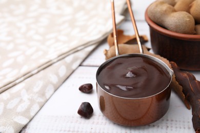 Photo of Measuring cup with tasty tamarind sauce and fresh pods on white wooden table. Space for text