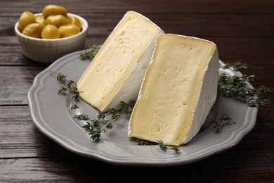 Photo of Pieces of tasty camembert cheese and thyme on wooden table, closeup