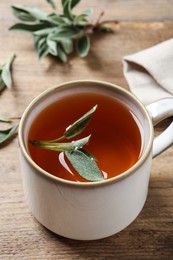 Photo of Cup of aromatic sage tea with fresh leaves on wooden table