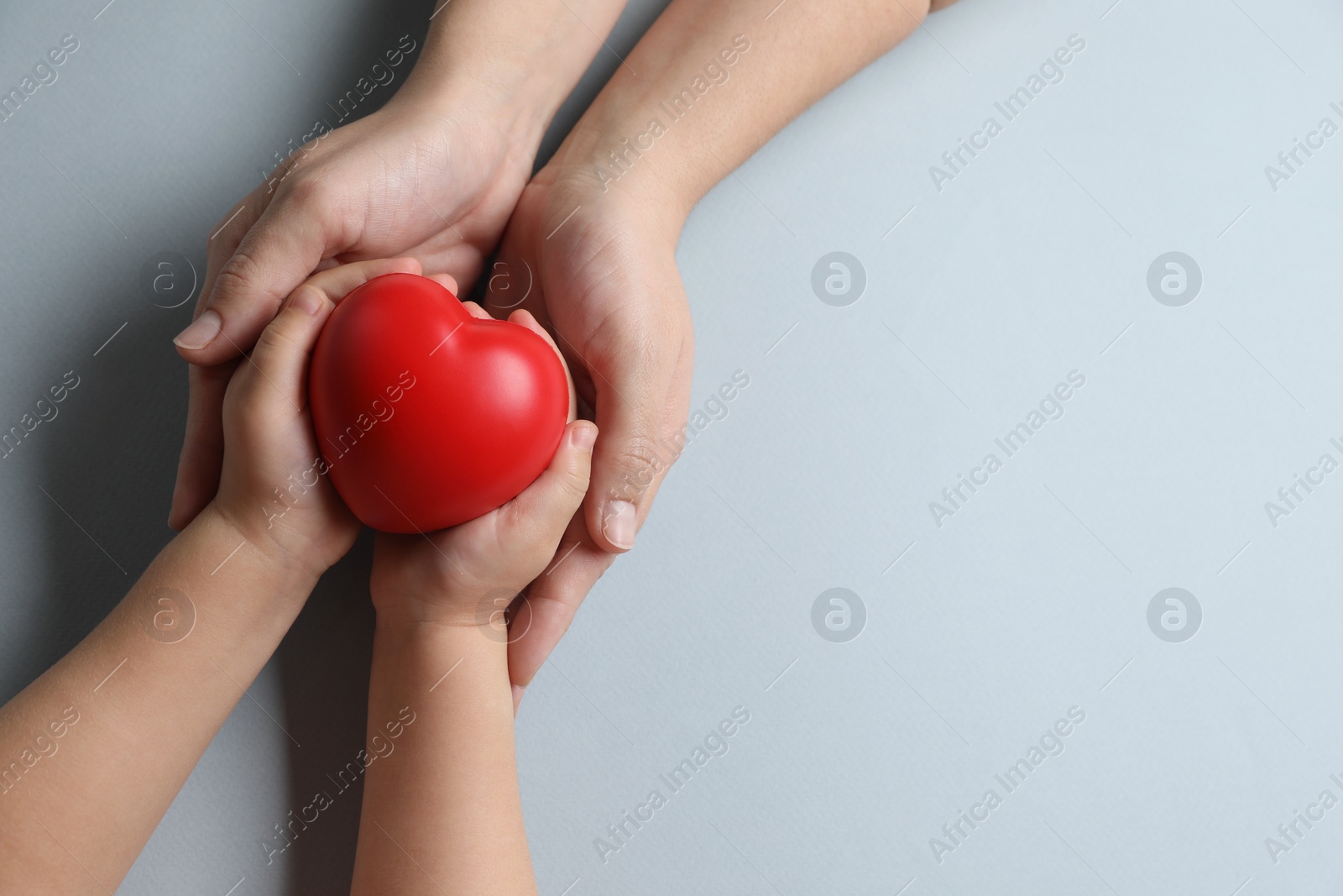 Photo of Mother and her child holding red decorative heart on gray background, top view. Space for text