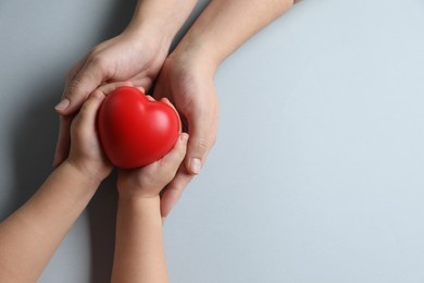 Mother and her child holding red decorative heart on gray background, top view. Space for text