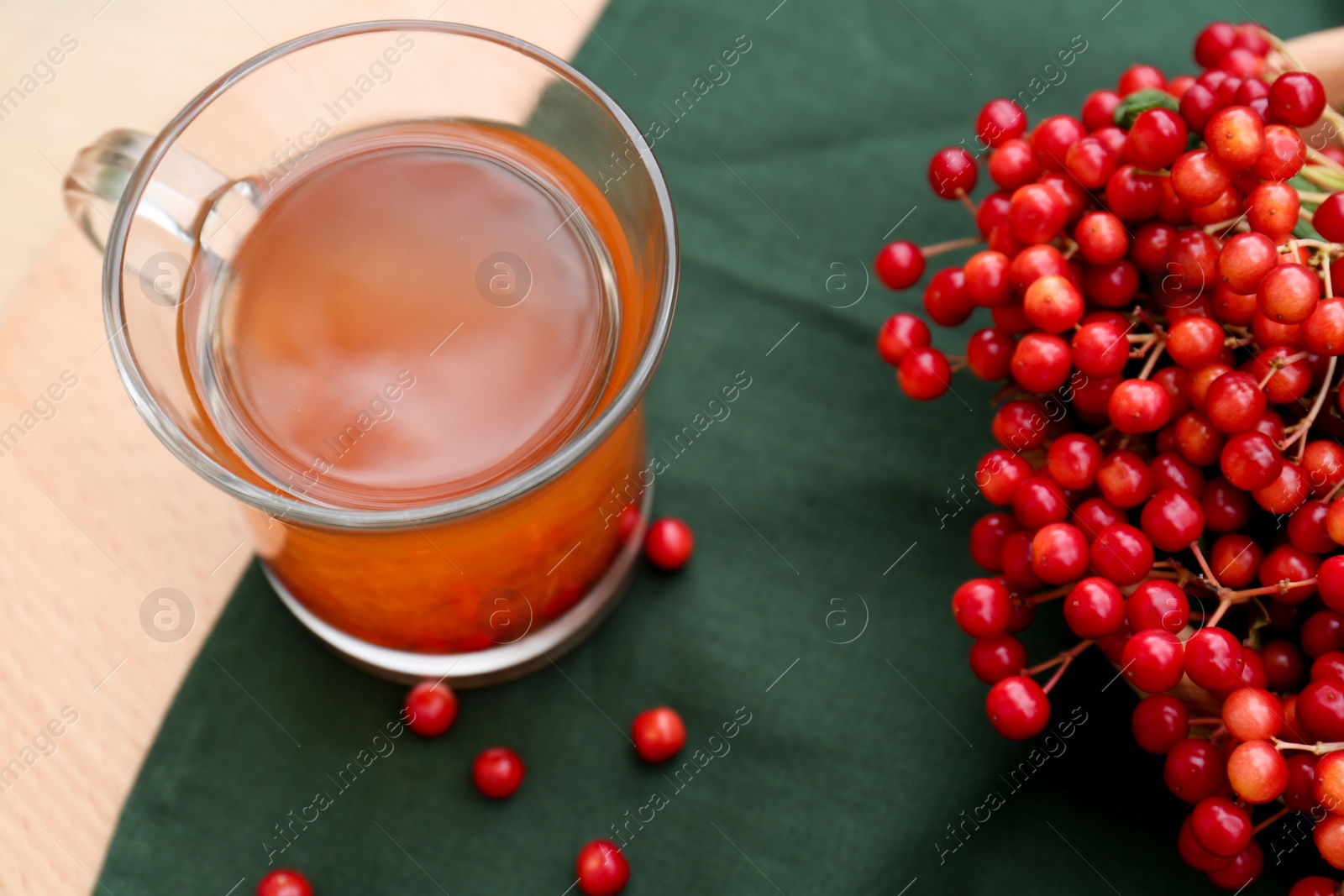 Photo of Cup of tea and fresh ripe viburnum berries on wooden table