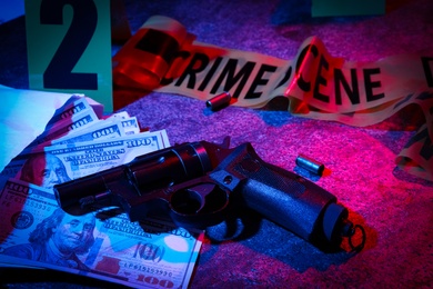 Money and gun on stone table, toned in red and blue. Crime scene