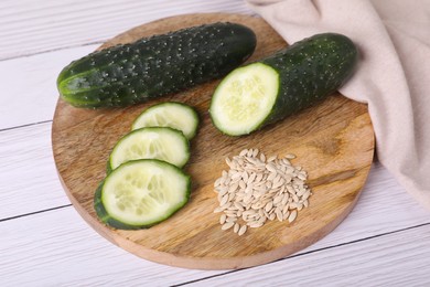 Photo of Pile of vegetable seeds and fresh cucumbers on white wooden table