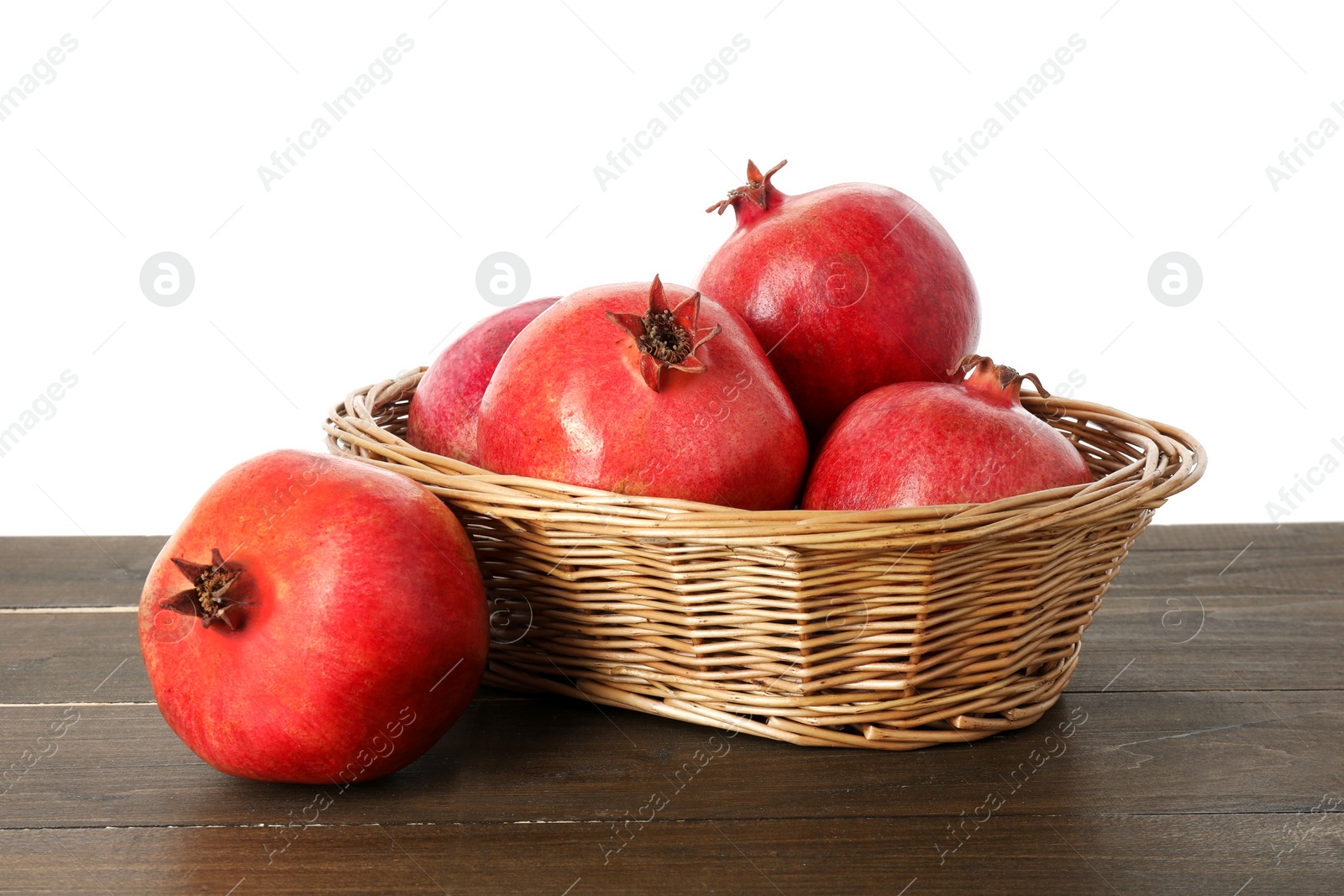 Photo of Fresh pomegranates in wicker basket on wooden table against white background