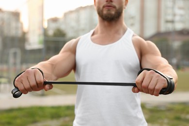 Muscular man doing exercise with elastic resistance band outdoors, closeup