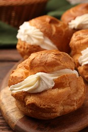 Photo of Delicious profiteroles with cream filling on wooden table, closeup
