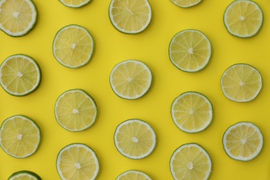 Photo of Slices of fresh juicy limes on yellow background, flat lay