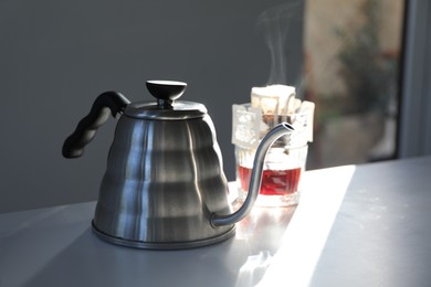 Photo of Glass with drip coffee bag and kettle on light grey table