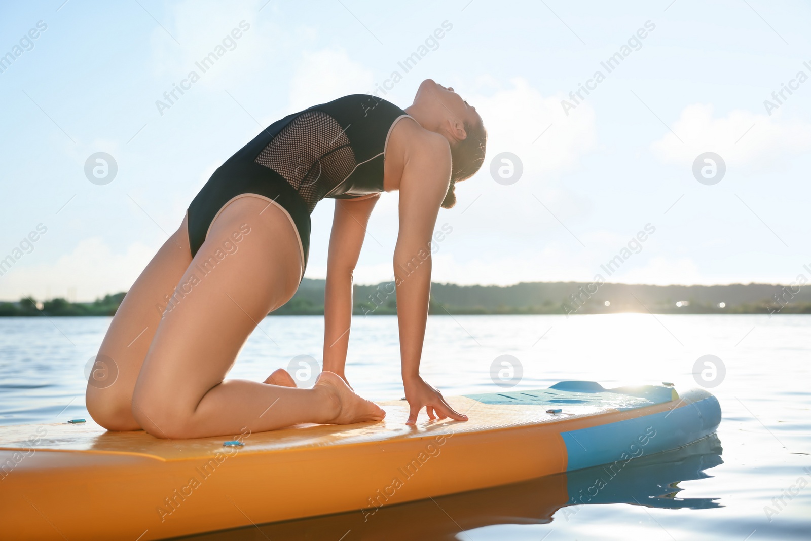 Photo of Young woman practicing yoga on color SUP board on river at sunset