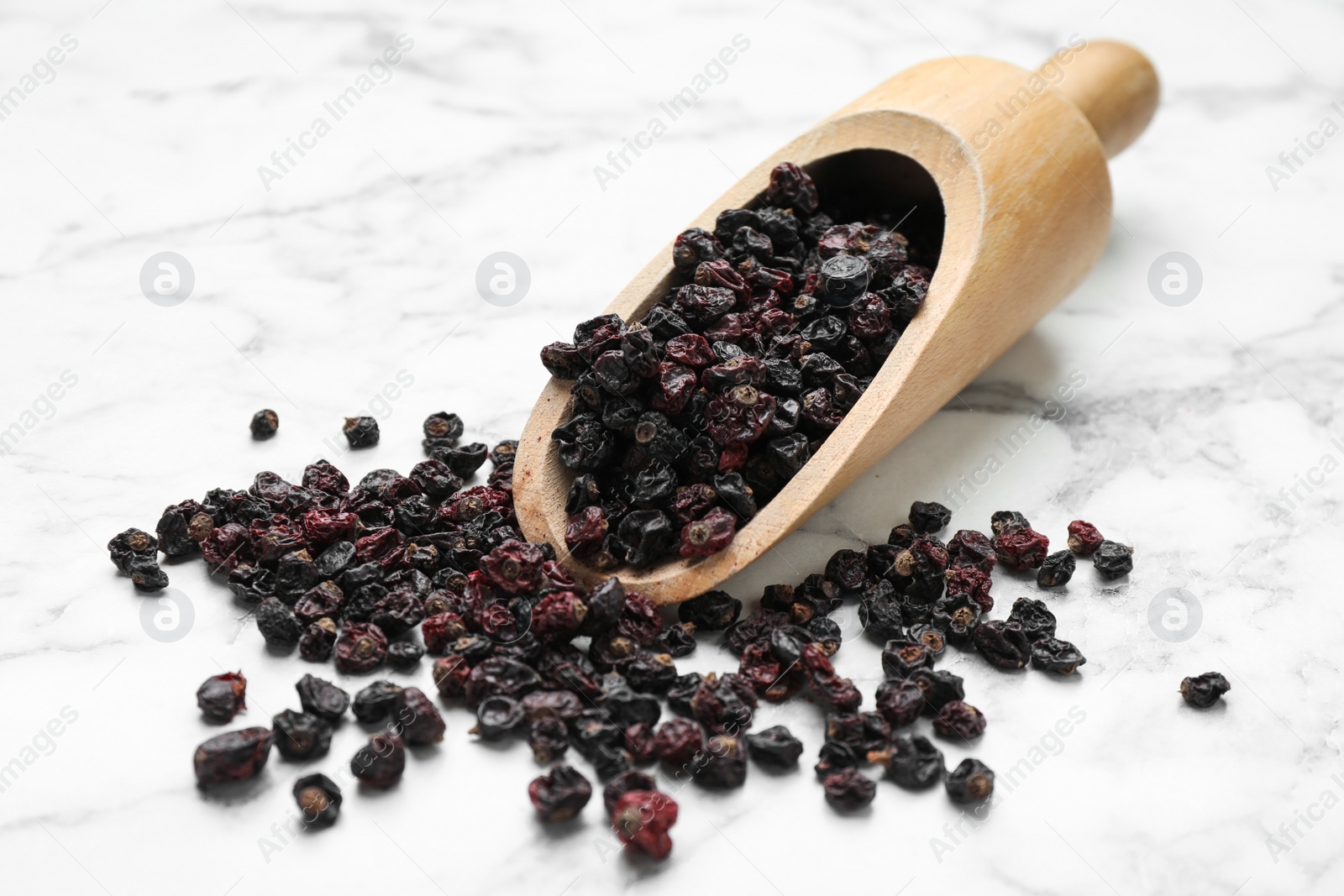 Photo of Wooden scoop with dried black currant berries on white marble table