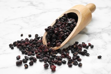 Wooden scoop with dried black currant berries on white marble table