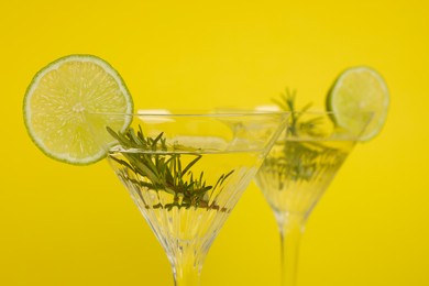Martini glasses of refreshing cocktail with lemon slices and rosemary on yellow background, closeup