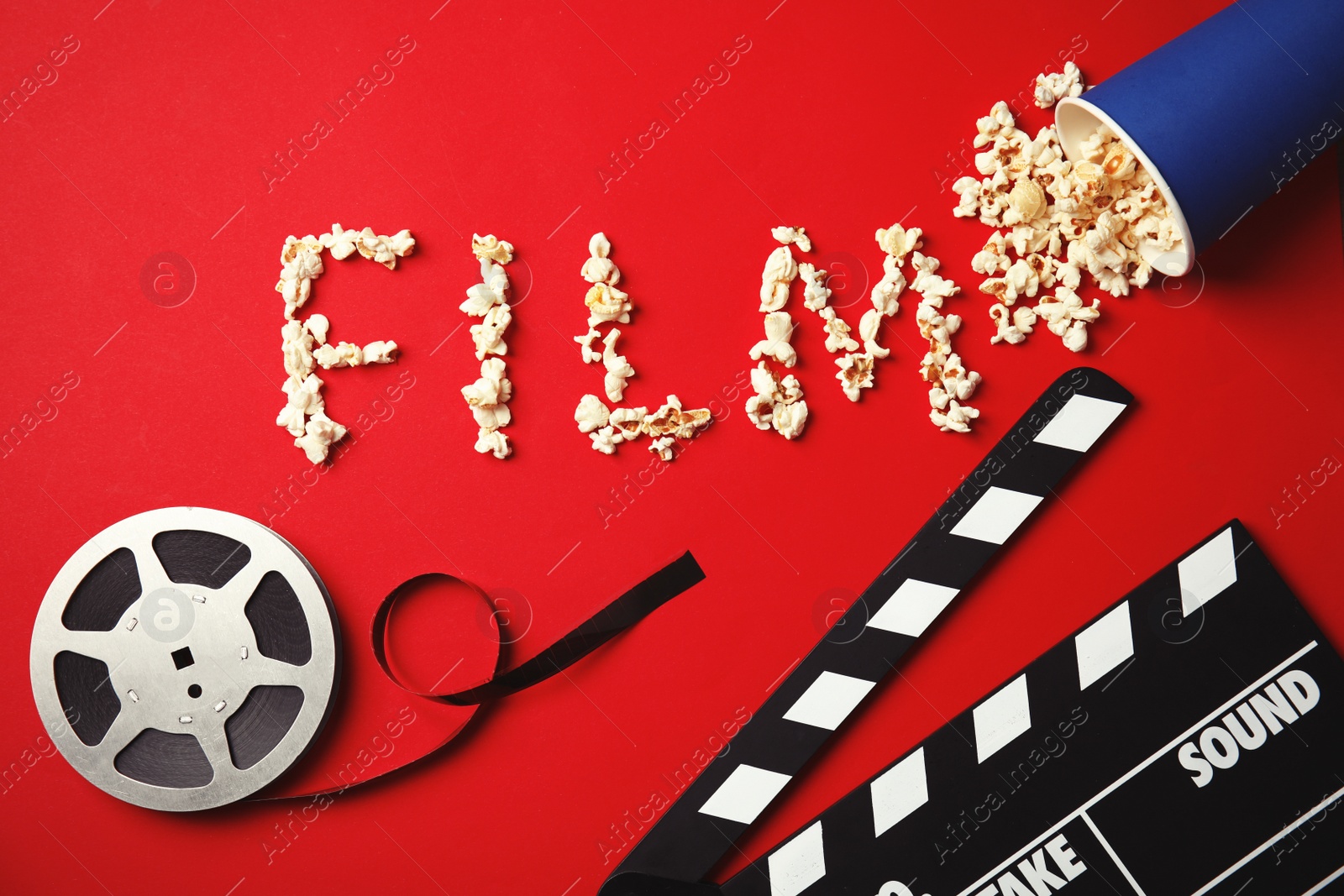 Photo of Flat lay composition with word FILM made of popcorn, reel and clapperboard on color background. Cinema snack