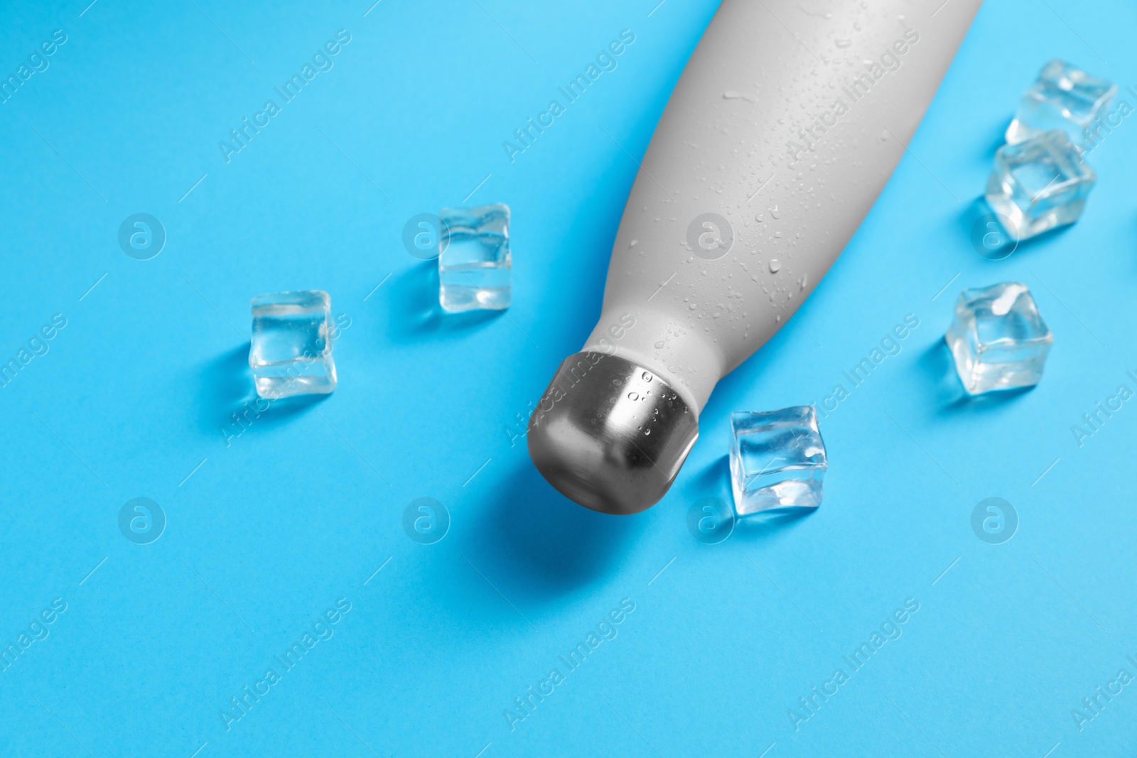 Photo of Stylish thermo bottle with water drops and ice cubes on light blue background, above view