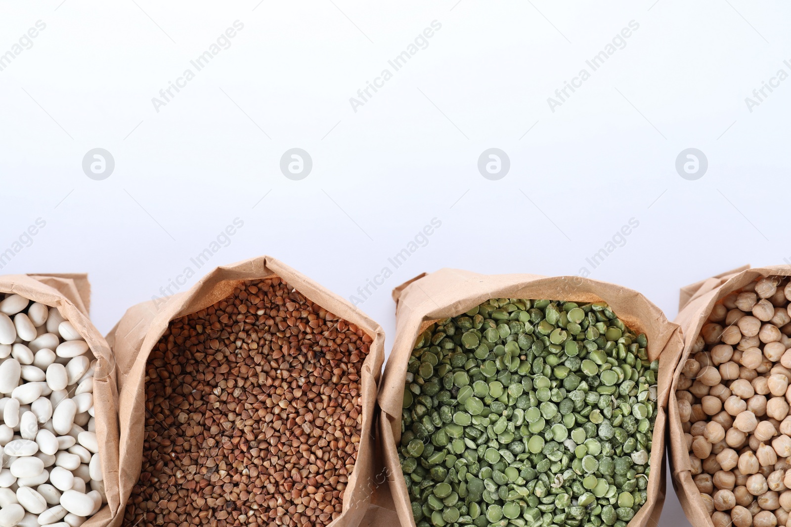 Photo of Different types of legumes  and cereals in paper bags on white background, top view. Organic grains