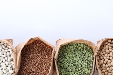 Different types of legumes  and cereals in paper bags on white background, top view. Organic grains