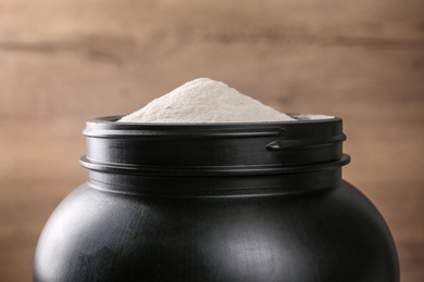 Photo of Black jar full of protein powder on brown background, closeup