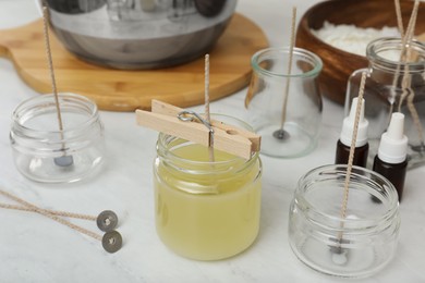 Photo of Glass jar with melted wax and wick on white kitchen table. Making homemade candle