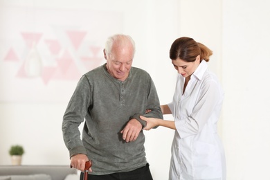 Elderly man with walking cane and female caregiver in room