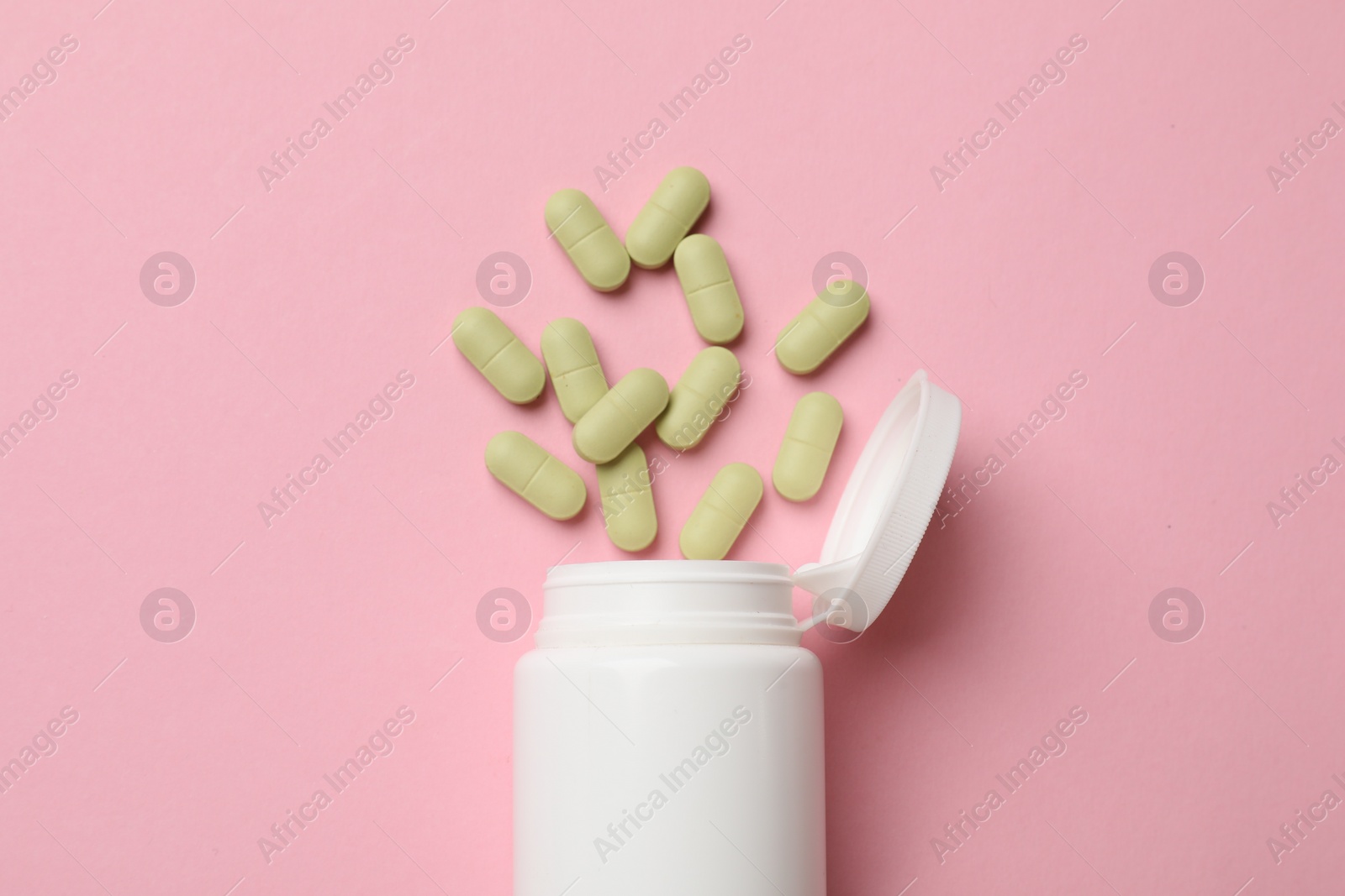 Photo of White bottle and different vitamin capsules on pink background, top view