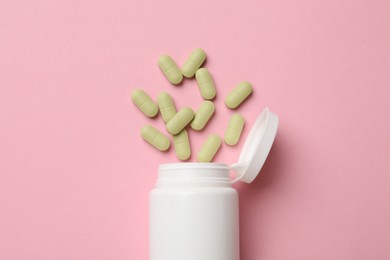 White bottle and different vitamin capsules on pink background, top view