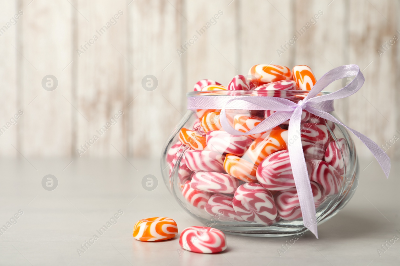 Photo of Sweet candies in glass jar on light grey table. Space for text