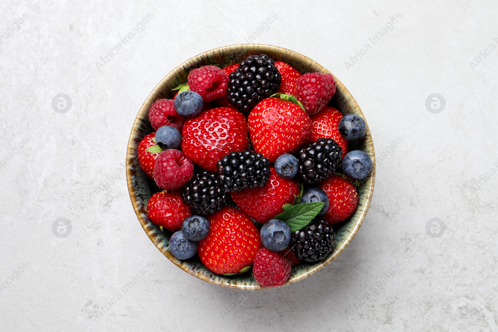 Different fresh ripe berries in bowl on light grey table, top view Photo of Different fresh ripe berries in bowl on light grey table, top view