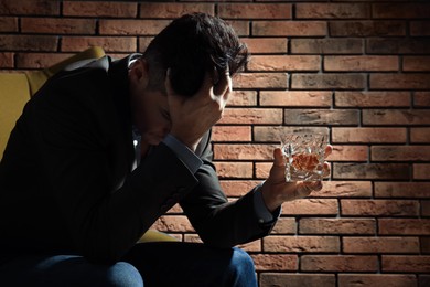Photo of Addicted man with glass of alcoholic drink in armchair near red brick wall