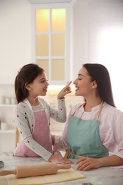 Mother with her cute little daughter having fun while rolling dough in kitchen