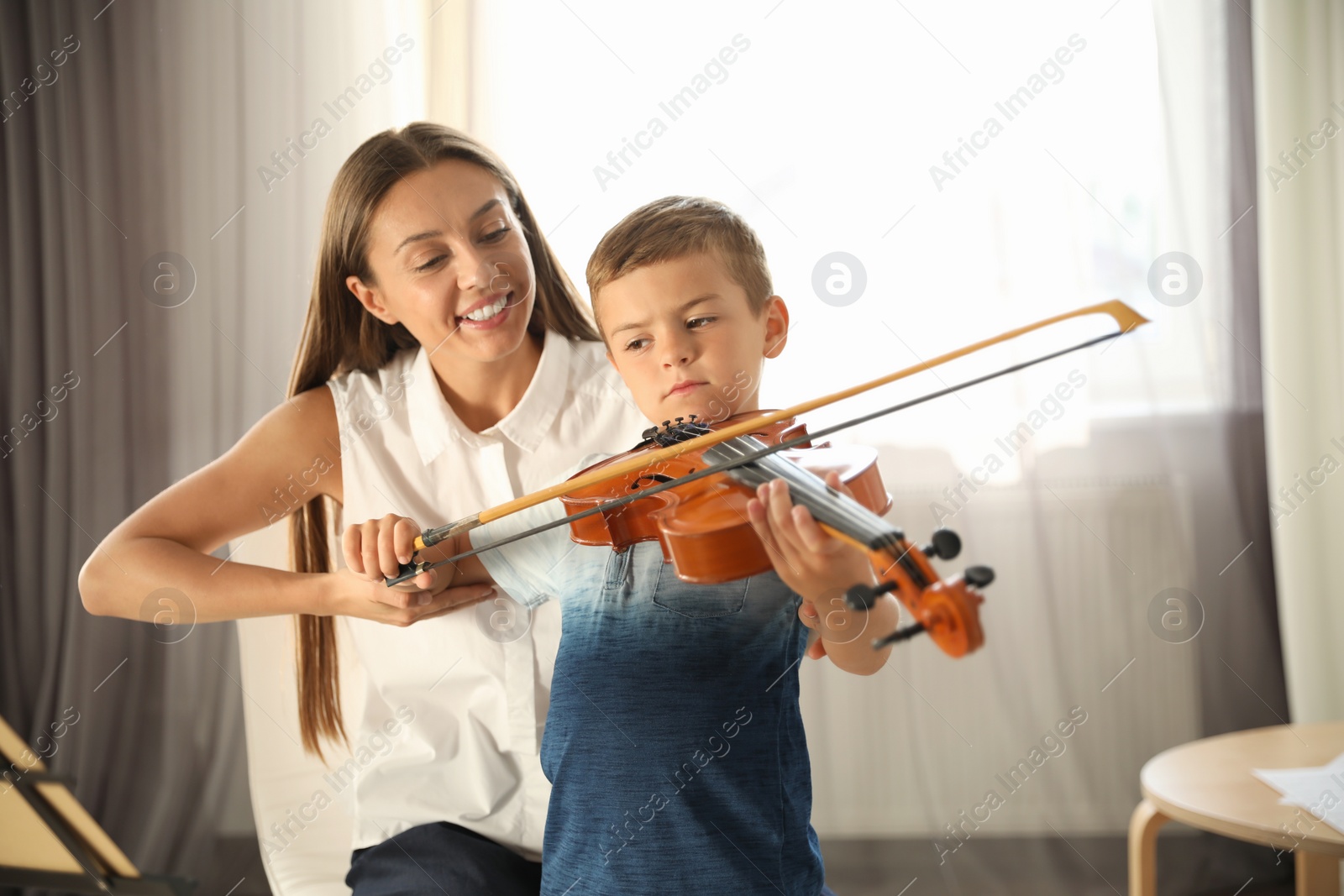 Photo of Young woman teaching little boy to play violin indoors