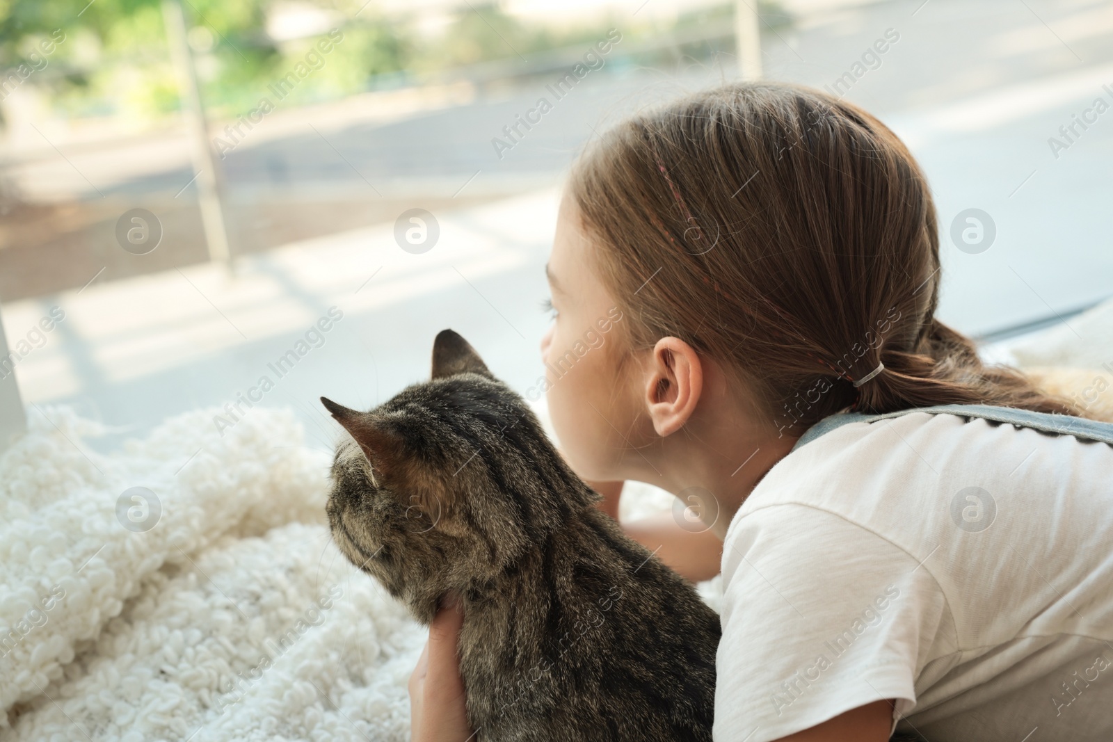 Photo of Cute little girl with her cat near window at home. Childhood pet