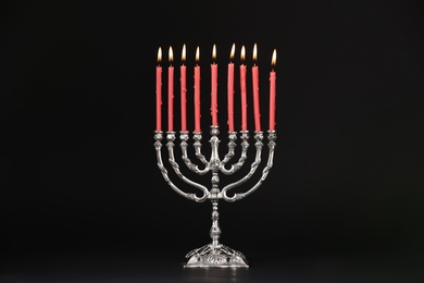 Photo of Silver menorah with burning candles on black background. Hanukkah celebration
